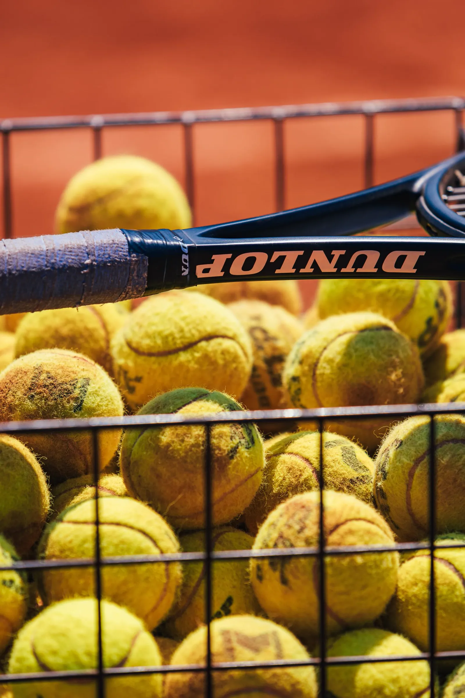 Basket full of yellow tennis balls by a court