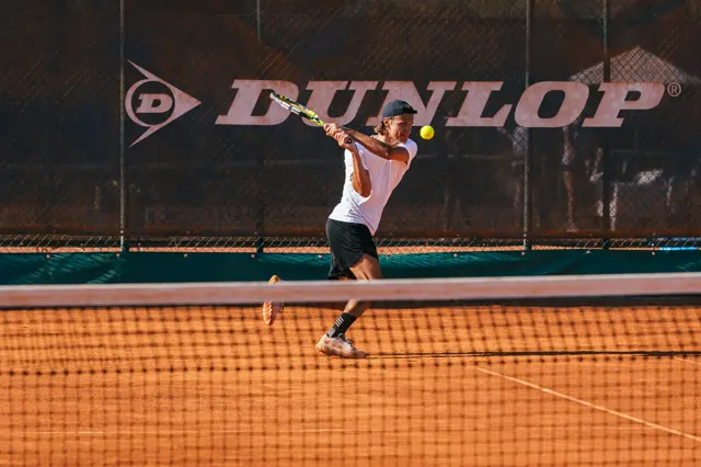 Player finishing a two-handed backhand on clay, racquet above the shoulder