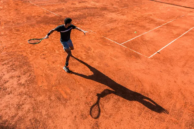 Player hitting a forehand from the back of a clay court, seen from above