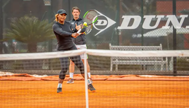 Player hitting a forehand volley at the net on clay with a coach in the background