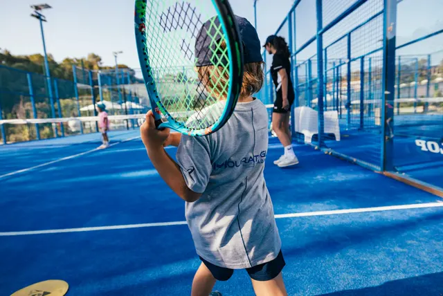 Niño pequeño en posición de espera, con la raqueta en la mano, en una pista de tenis