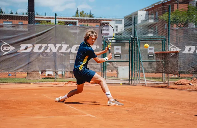 Player hitting a backhand slice on a red clay court