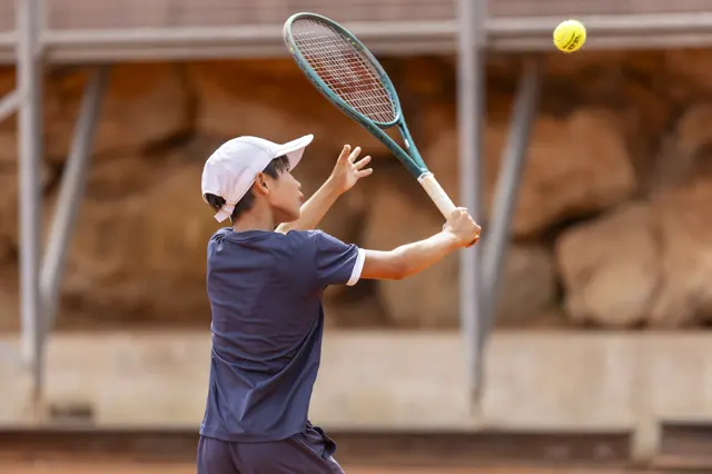 Young player hitting a high volley on a clay court