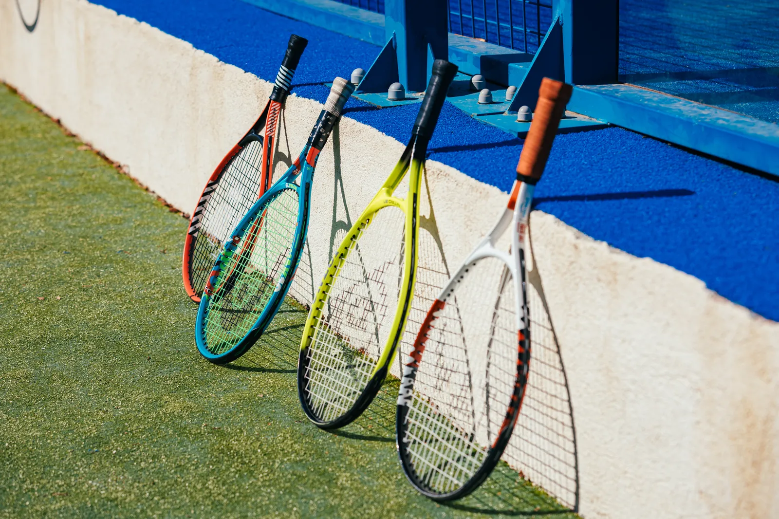Quatre raquettes de tennis appuyées contre un muret au bord d’un court