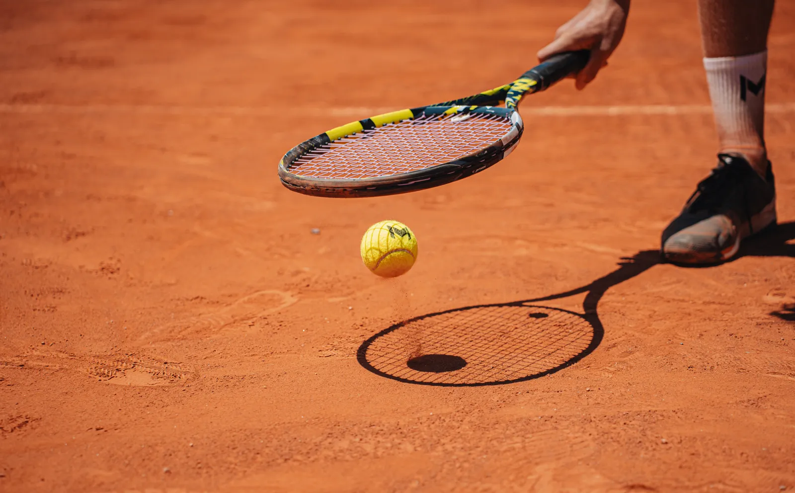 Raqueta de tenis sobre una bola que bota en una pista de tierra batida