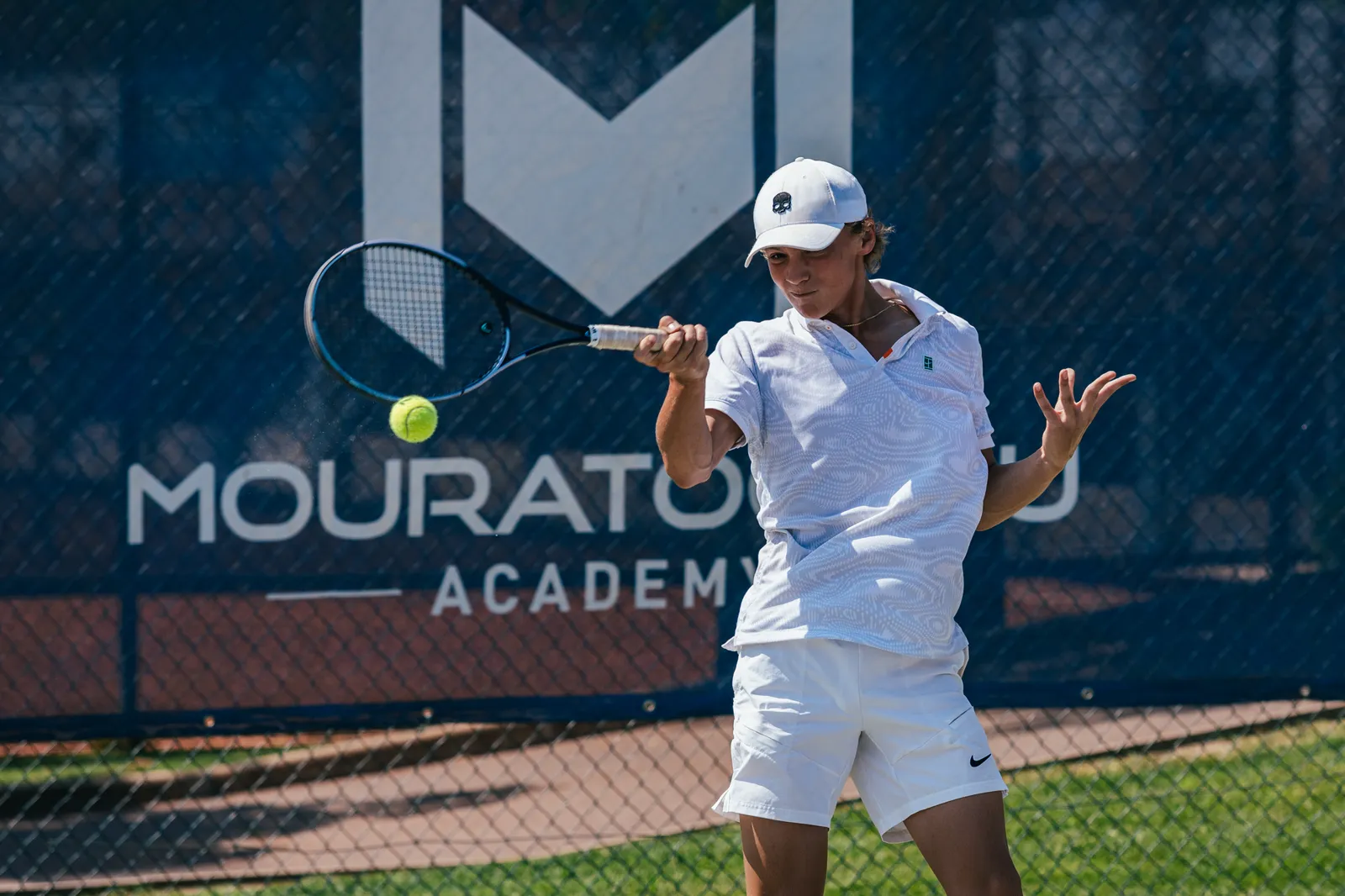 Young player hitting a forehand in front of a Mouratoglou Academy banner