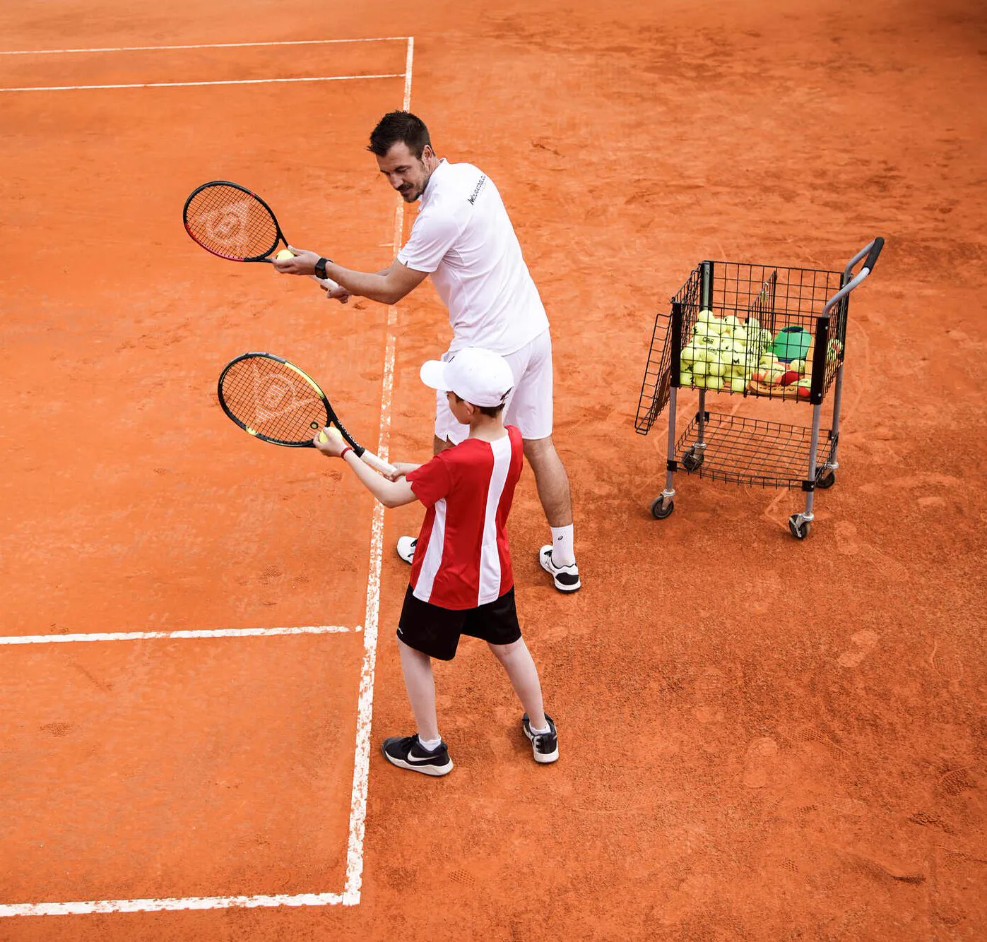 Coach montrant à un enfant la position de départ au service sur terre battue