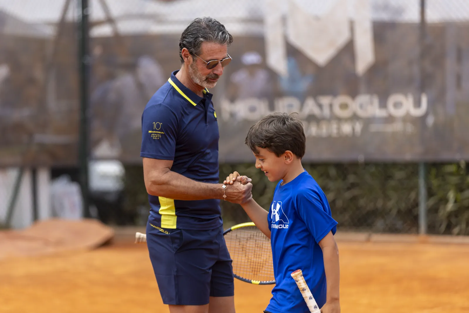 Entrenador rodeado de jóvenes jugadores en una pista de tenis