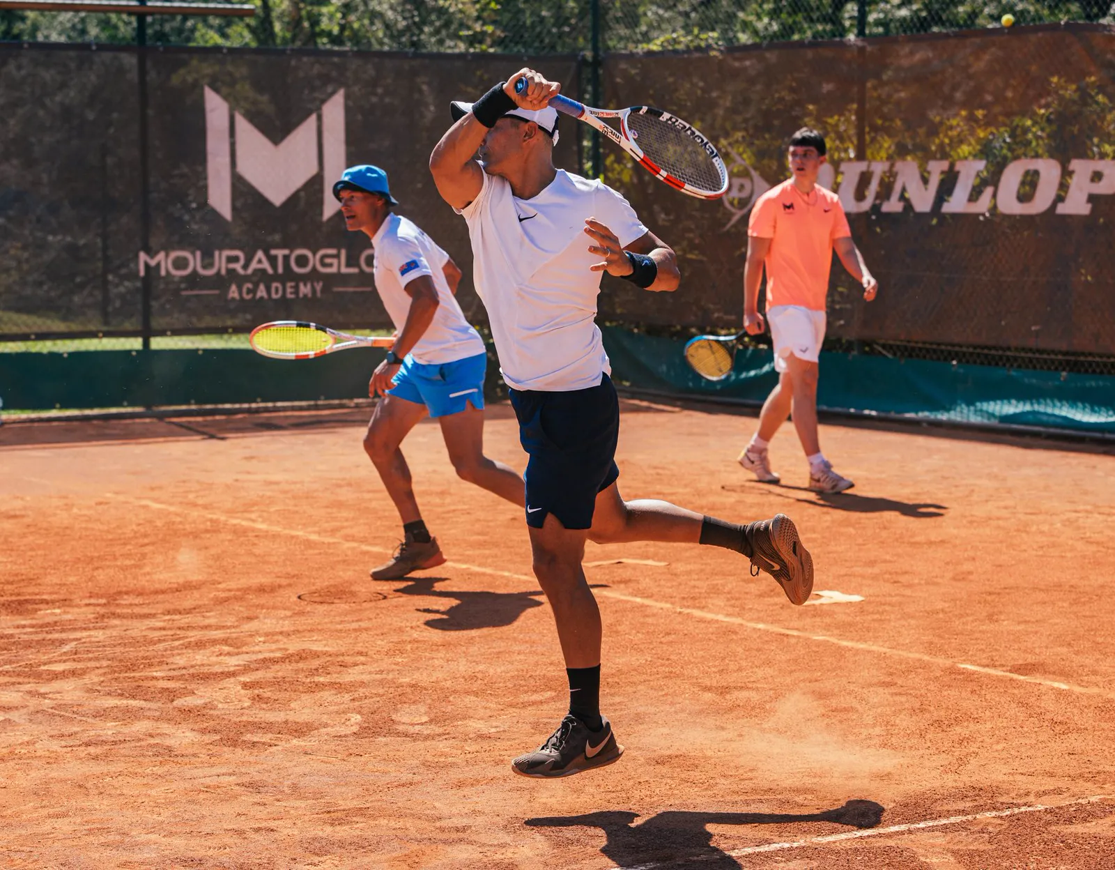 Joueur jouant une volée haute en double sur un court en terre battue de la Mouratoglou Academy