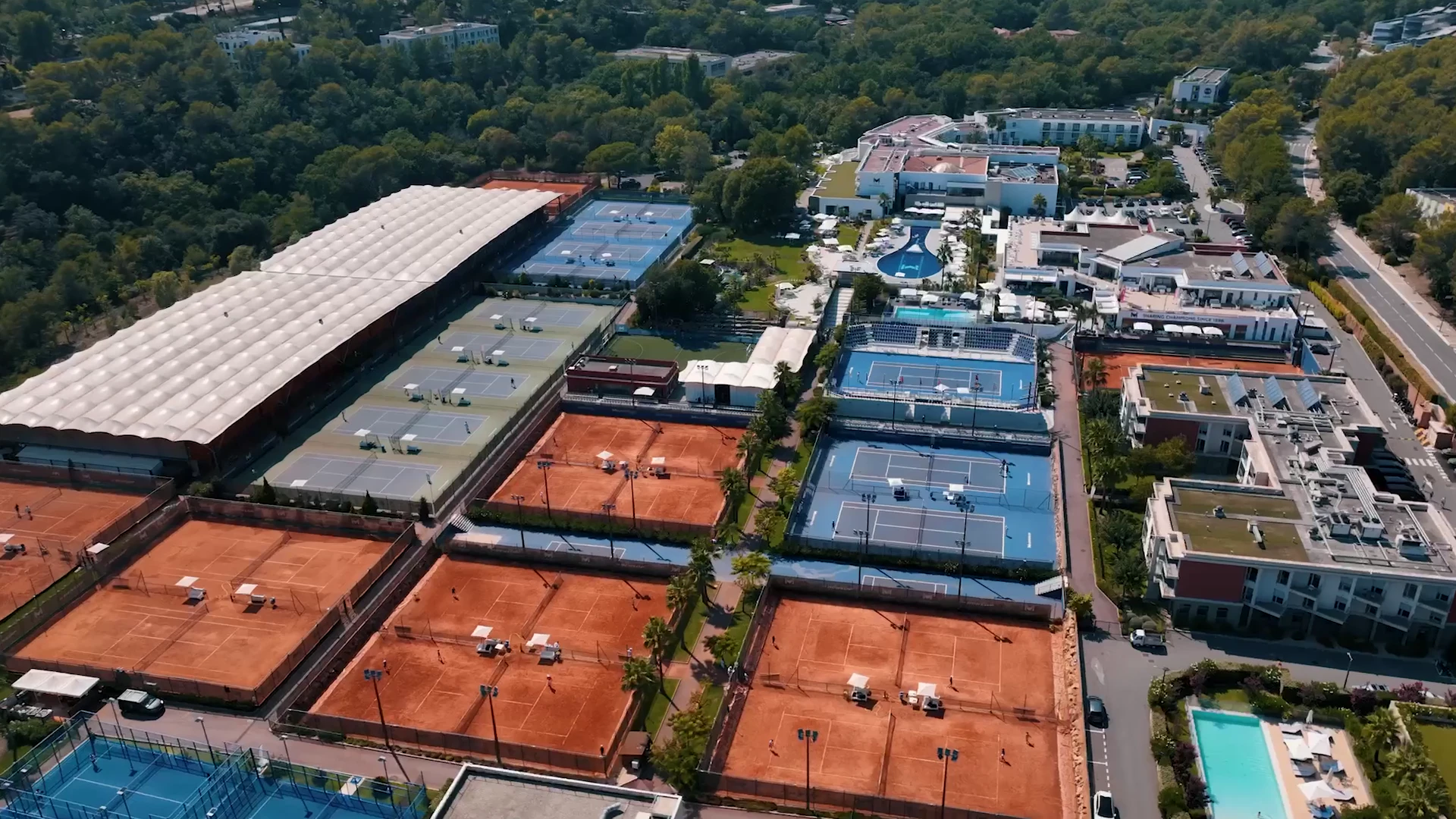 Luftaufnahme des Campus der Mouratoglou Academy mit Sand- und Hartplätzen und Gebäuden im Wald