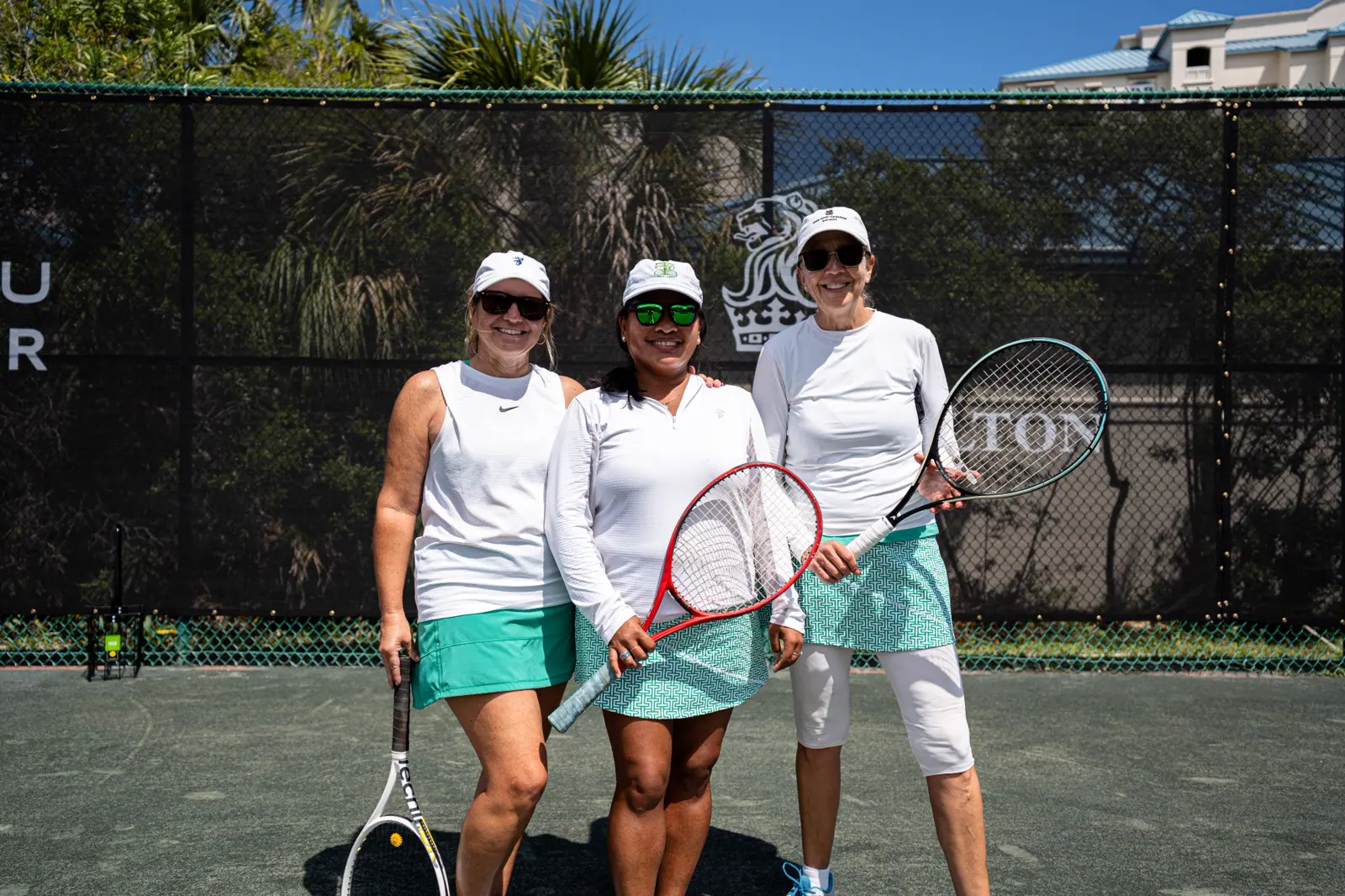 Drei erwachsene Frauen mit Tennisschlägern auf einem Außenplatz im Mouratoglou Tennis Center Amelia Island