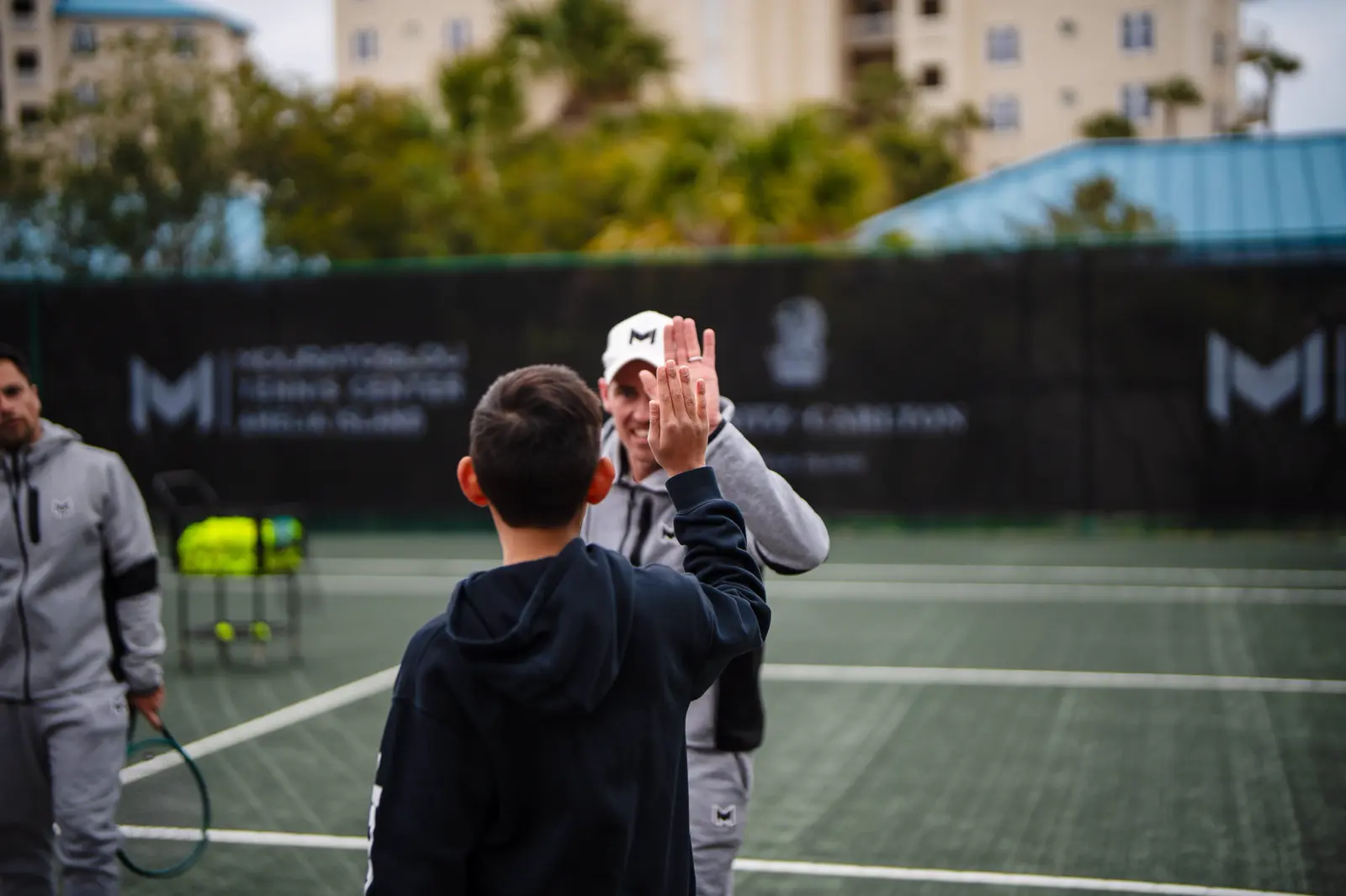Entrenador de tenis chocando los cinco con un joven jugador en la pista del Mouratoglou Tennis Center Amelia Island