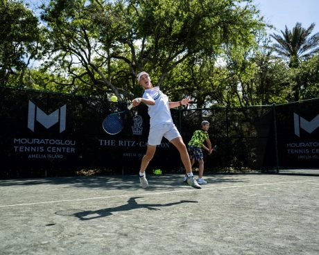Niño golpeando con fuerza una pelota en las pistas del Mouratoglou Tennis Center Amelia IslandUn joven jugador devuelve con potencia una pelota en las pistas del Mouratoglou Tennis Center Amelia Island. Esta imagen refleja la fuerza, la determinación y la alegría de competir que inspira la metodología Mouratoglou, que convierte el esfuerzo en confianza y pasión.