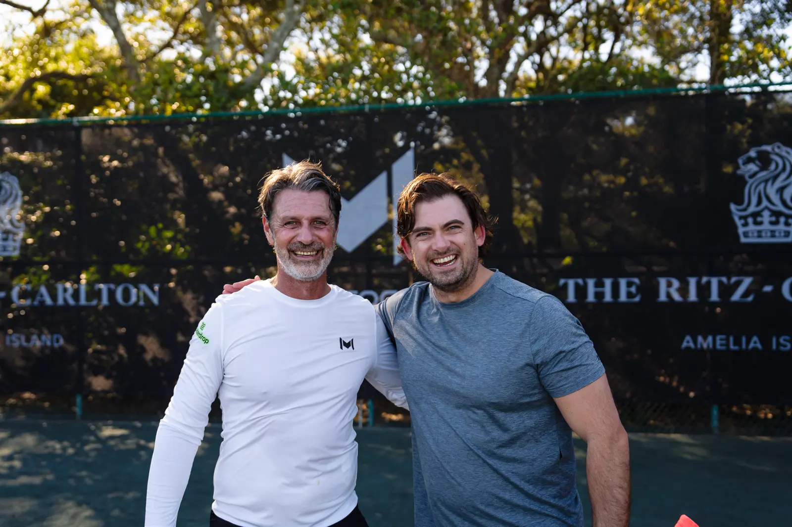 Patrick Mouratoglou posando con un jugador delante de los cortavientos con la marca Mouratoglou en Amelia Island