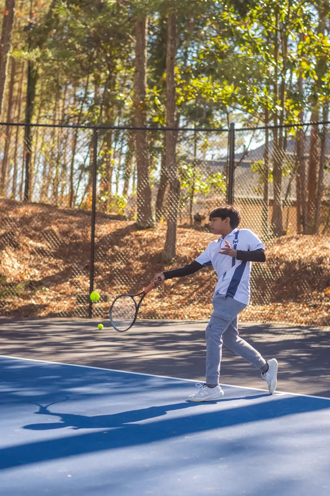 Junge schlägt eine Vorhand auf einem von Wald umgebenen Außenplatz in Atlanta.