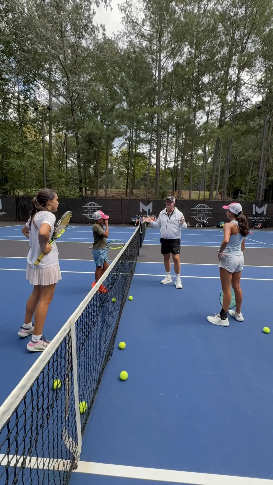 Tres niños en la red escuchando a su entrenador en la Mouratoglou Academy Atlanta