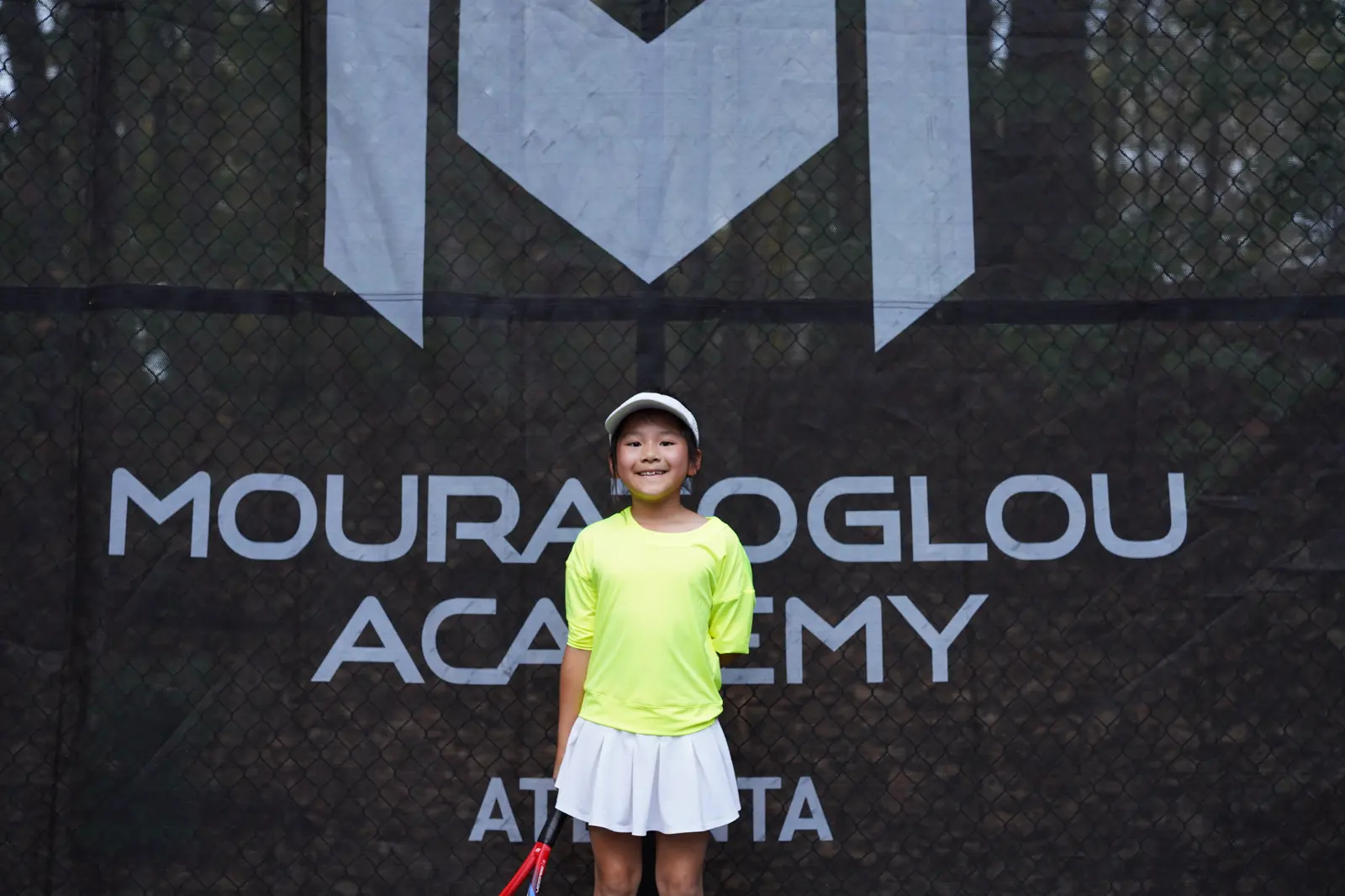 Niña sonriente delante de los cortavientos Mouratoglou en la Mouratoglou Academy Atlanta