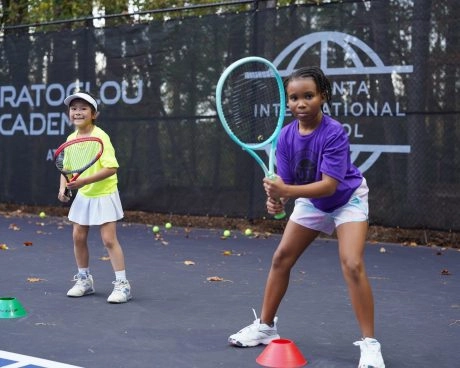 Zwei junge Tennisspieler trainieren mit ihrem Coach auf dem Platz an der Mouratoglou Academy Atlanta