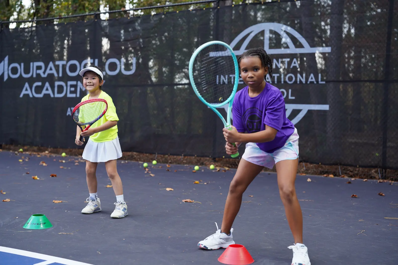 Dos jóvenes jugadores de tenis entrenando con su entrenador en la Mouratoglou Academy Atlanta