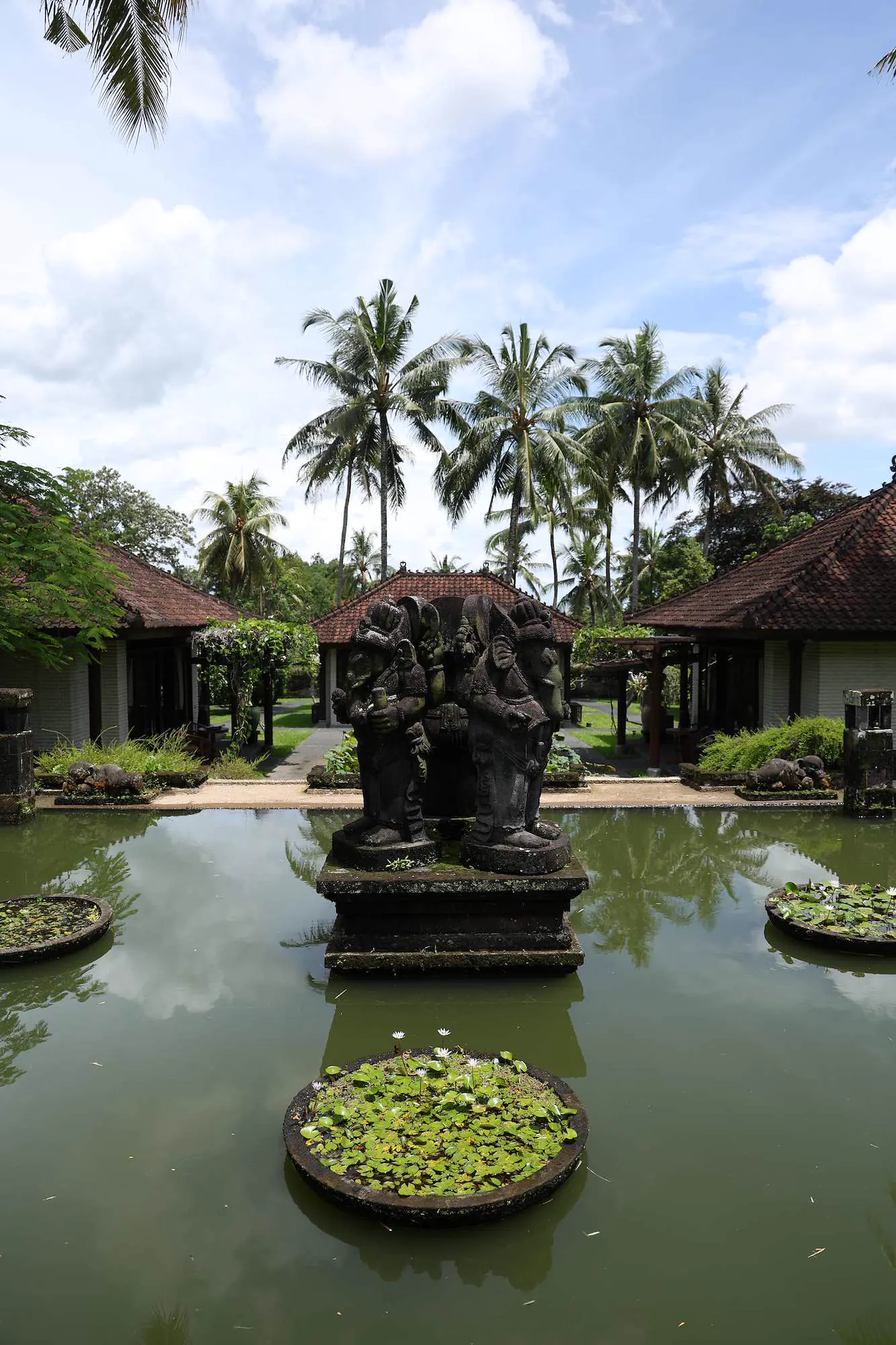 Statua balinese tradizionale in pietra in uno stagno di loto nei giardini del Kula Mani.