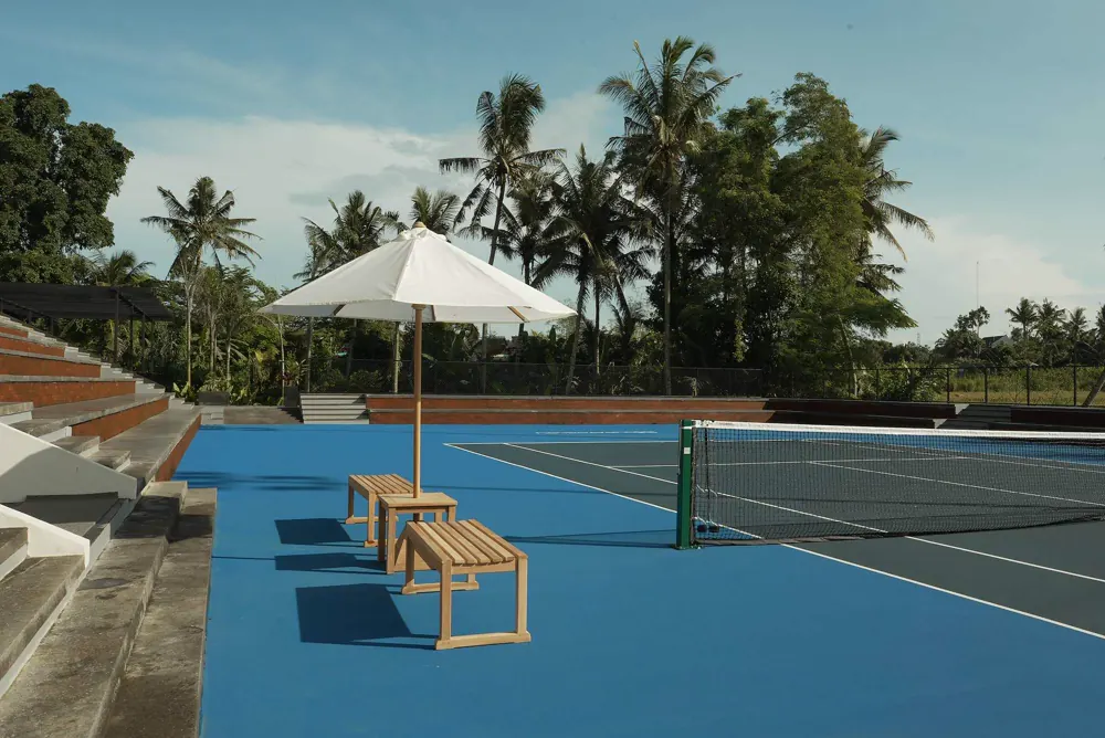 Campo da tennis in cemento all’aperto con panchina ombreggiata e palme al Mouratoglou Tennis Center Bali.