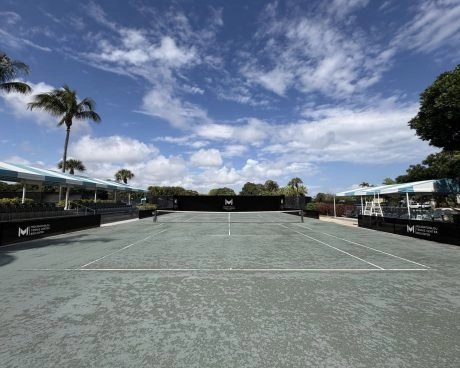 Reihe von Außentennisplätzen unter blauem Himmel im Mouratoglou Tennis Center Boca Raton.