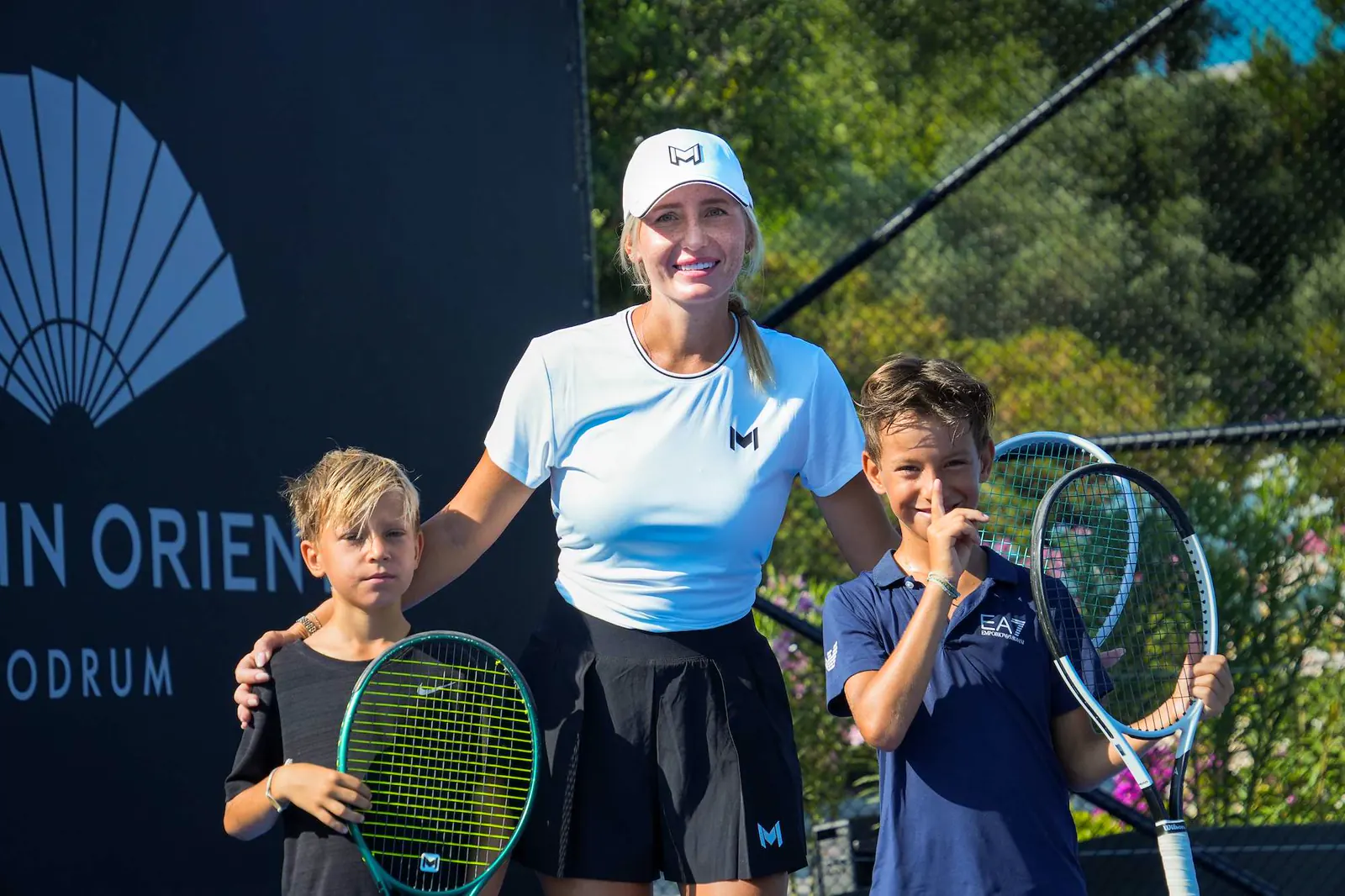 Entrenador Mouratoglou sonriendo con jóvenes jugadores en la pista en Bodrum.
