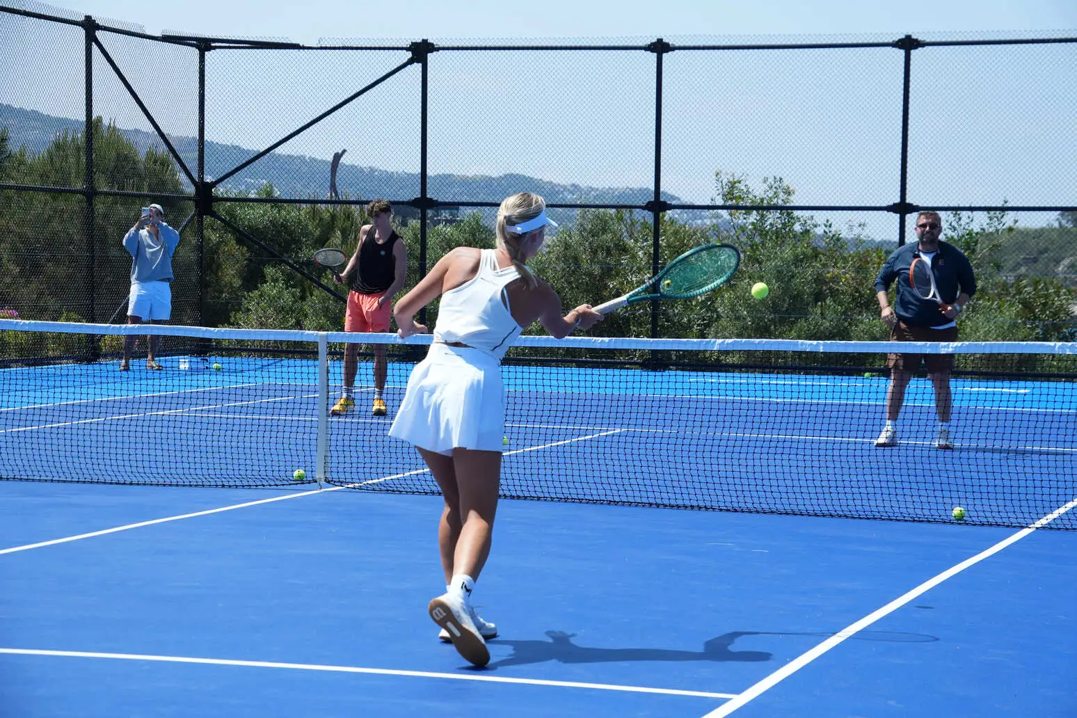 Four players during a group tennis lesson on a blue court in Bodrum