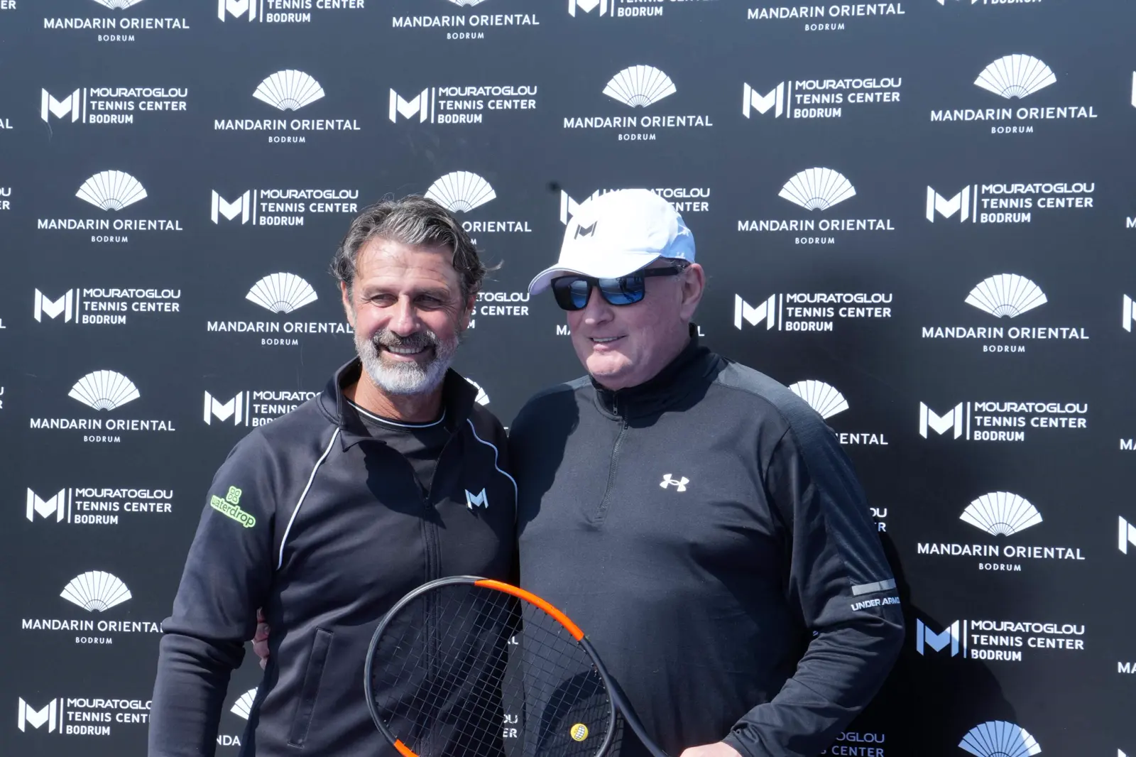 Patrick Mouratoglou with a guest in front of the Mouratoglou Tennis Center Bodrum wall