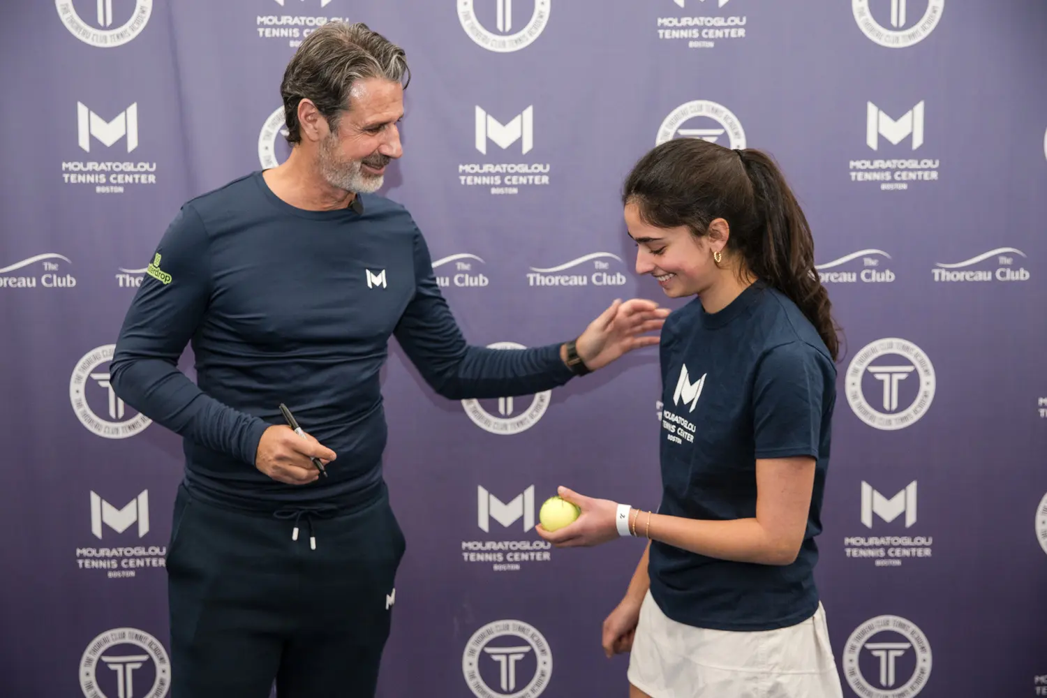 Patrick Mouratoglou firma una pallina da tennis per un giovane giocatore al Mouratoglou Tennis Center Boston.