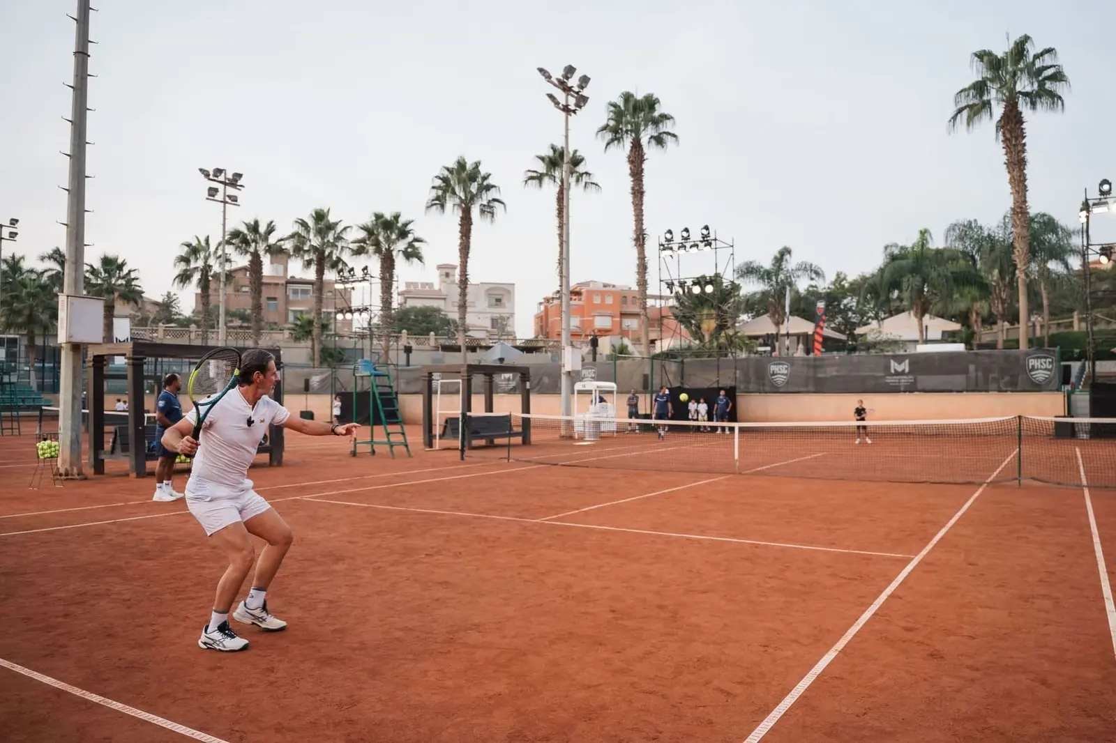 Jugador peloteando en una pista central de tierra batida iluminada del Mouratoglou Tennis Center Palm Hills Cairo.