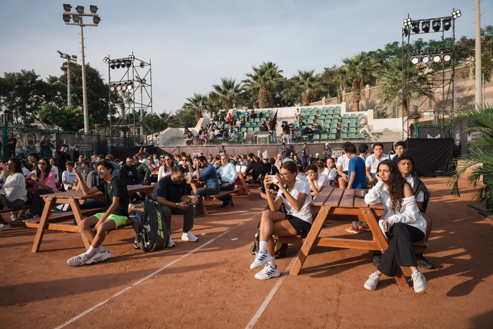 Invitados sentados en las pistas de tierra batida durante un evento comunitario en el Mouratoglou Tennis Center Palm Hills Cairo.
