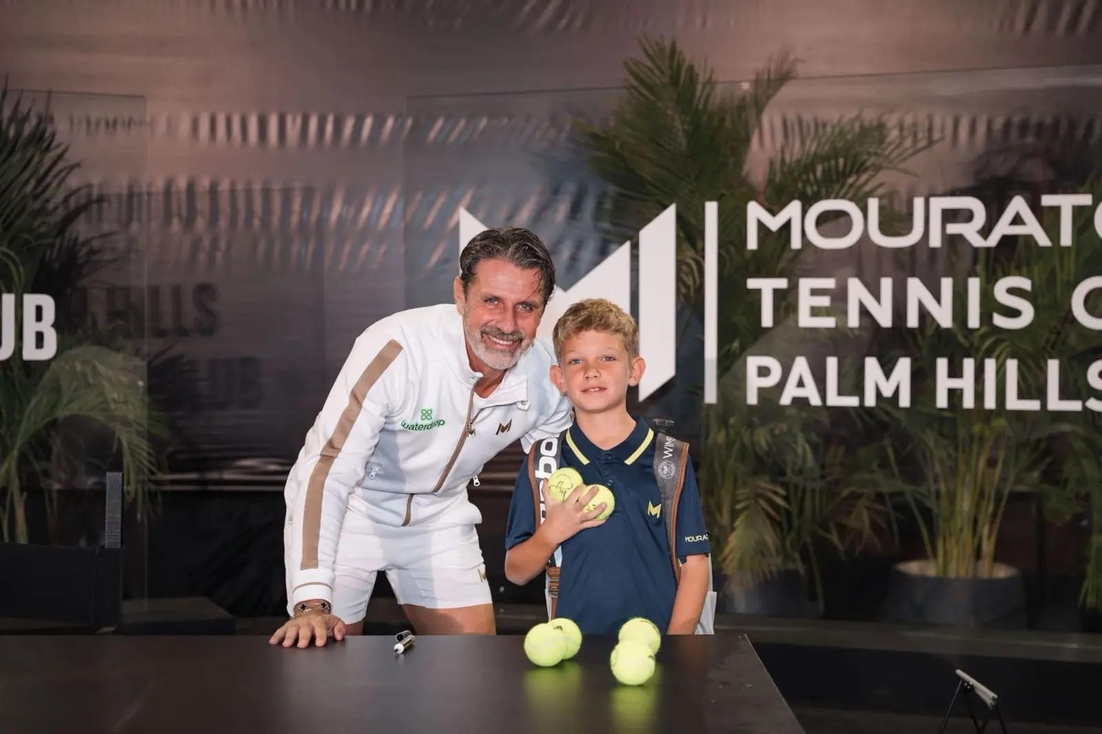 Patrick Mouratoglou mit einem Jungen, der signierte Tennisbälle hält, in Palm Hills