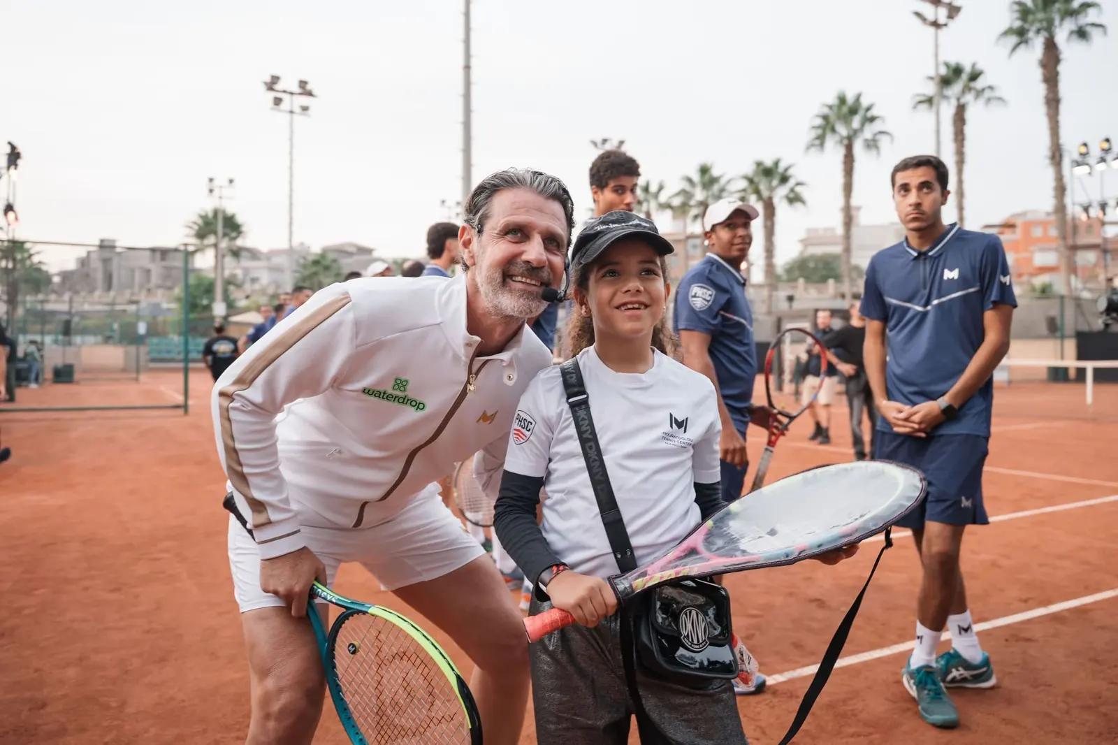 Patrick Mouratoglou con un joven jugador que sostiene una raqueta en una pista de tierra batida en Palm Hills, El Cairo.