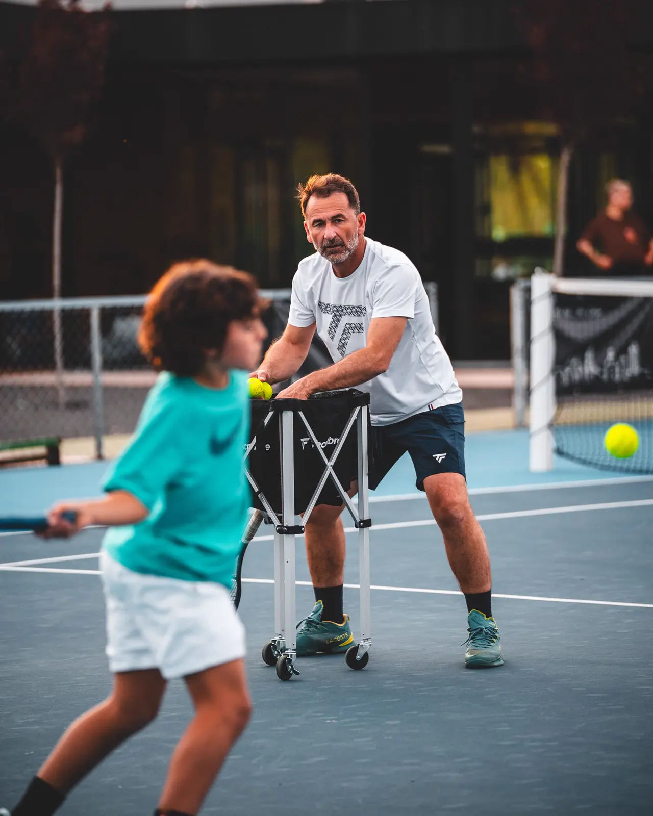 Coach avec un panier de balles entraînant un jeune joueur à Calatrava