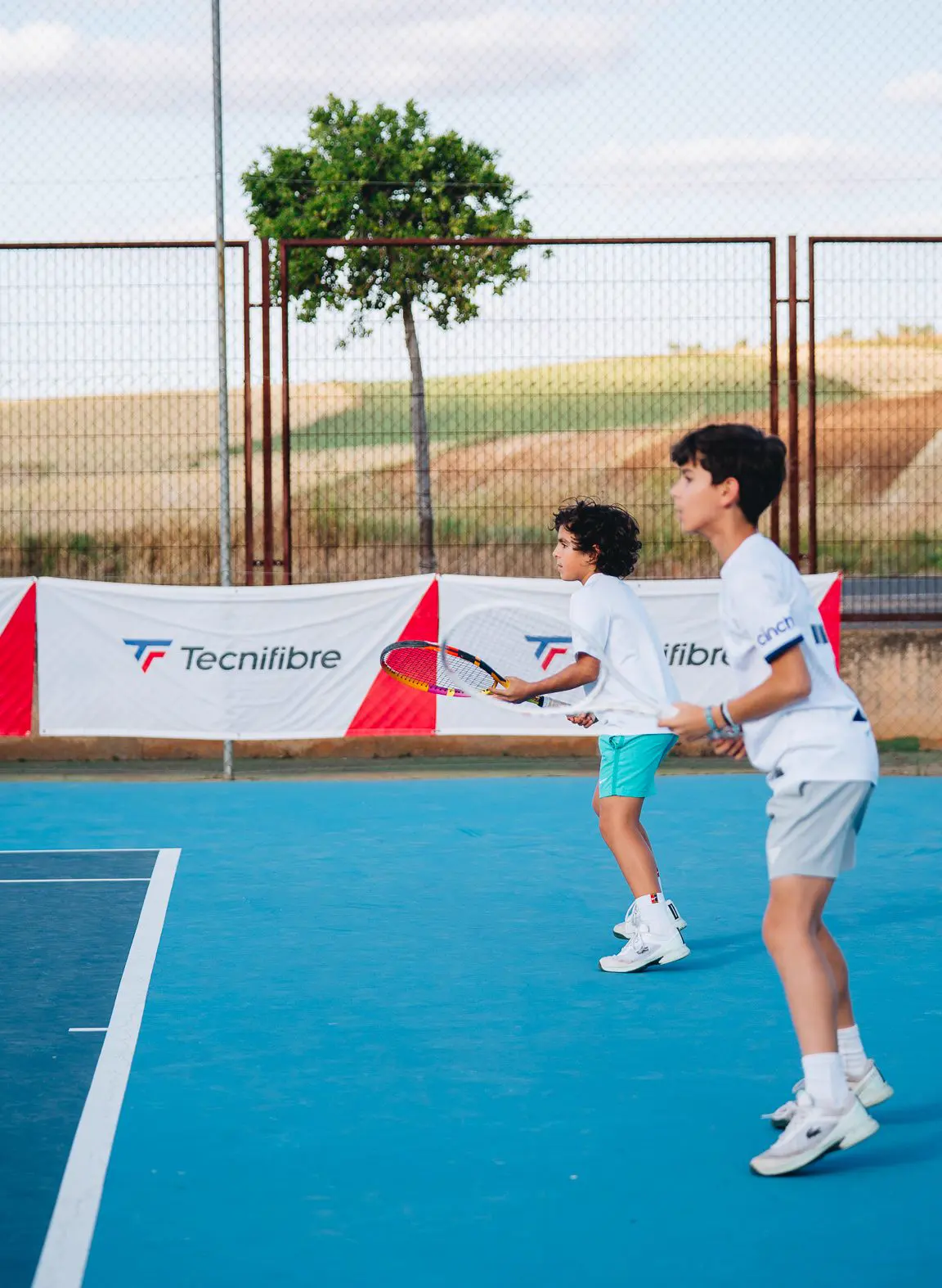 Coach führt einen jungen Spieler auf einem Hartplatz in Calatrava an das Tennis heran.