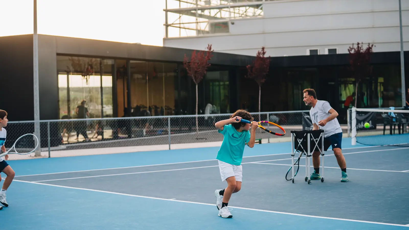 Coach spielt einem jungen Spieler Bälle aus dem Ballwagen zu, im Mouratoglou Tennis Center Calatrava.