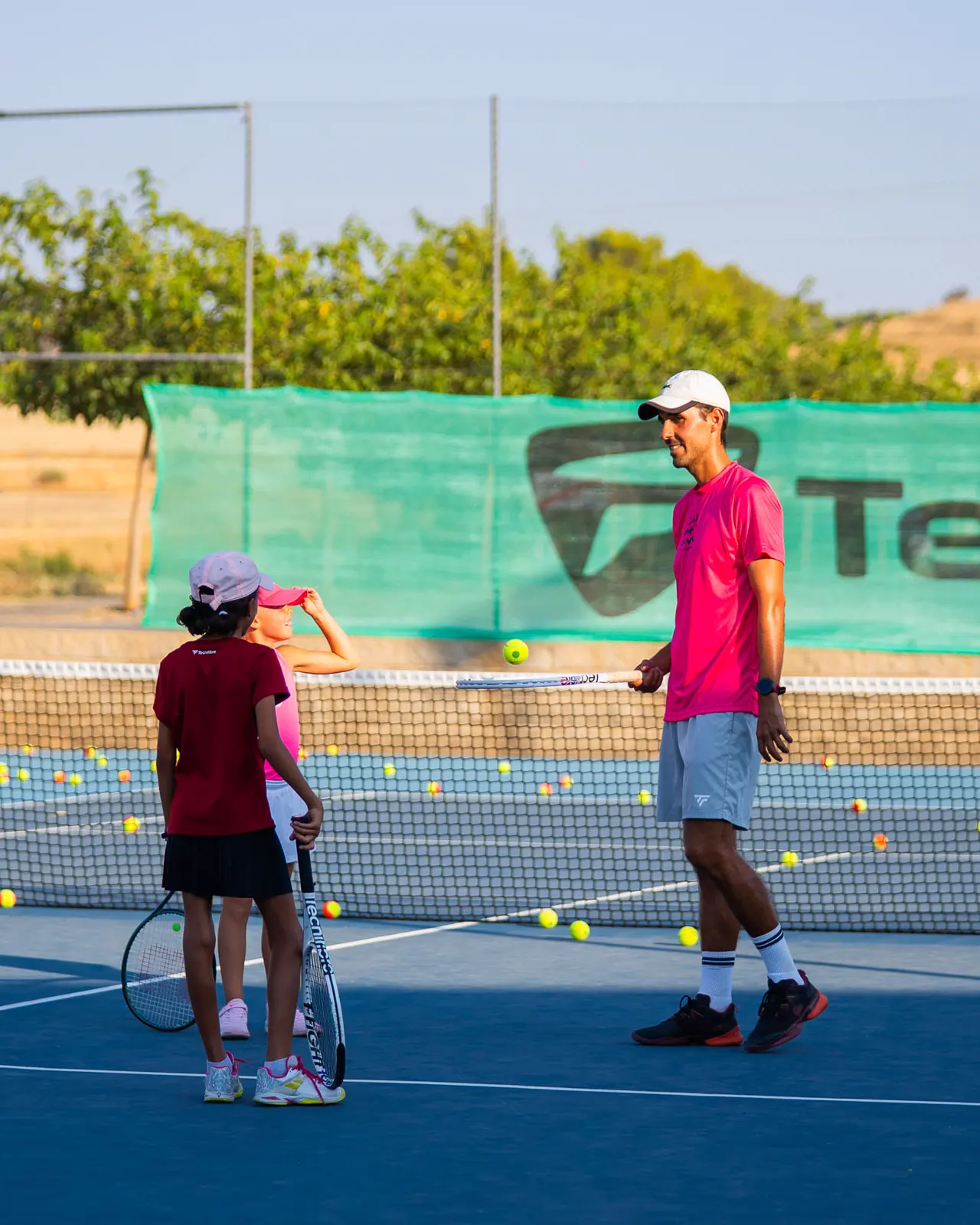 Coach feeding balls to a junior on a hard court in Calatrava