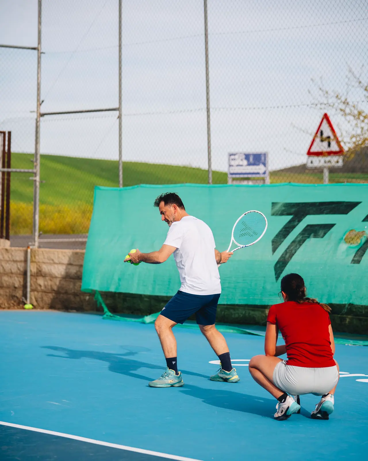 Coach kneeling beside a young player to correct a stroke in Calatrava