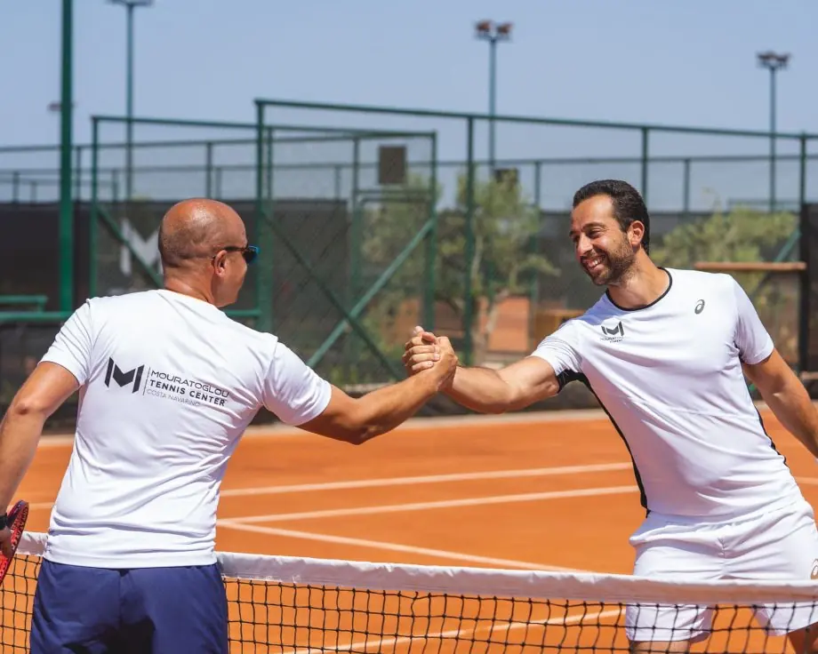 Due giocatori si stringono la mano a rete su un campo in terra battuta al Mouratoglou Tennis Center Costa Navarino.