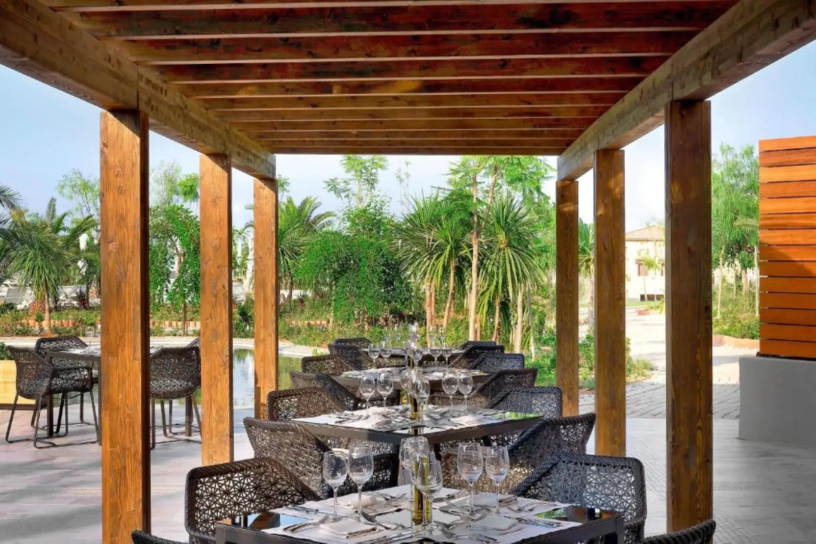 Terrazza di un ristorante all’aperto con tavoli apparecchiati affacciata sui giardini del The Westin Resort Costa Navarino.