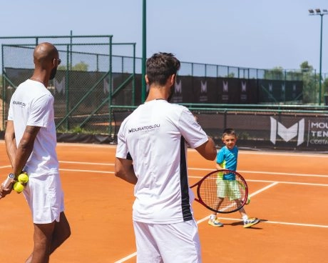 Coach di tennis che guidano un bambino durante l’allenamento su un campo in terra battuta