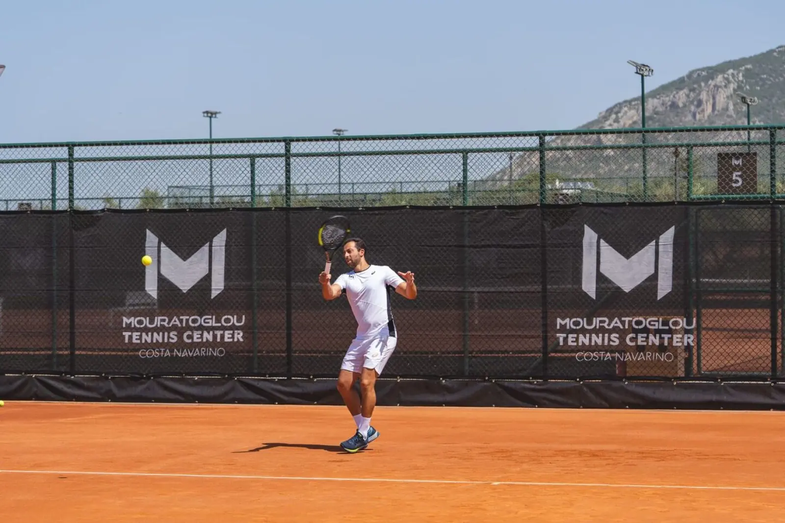 Giocatore che colpisce un dritto su un campo in terra battuta al Mouratoglou Tennis Center Costa Navarino.