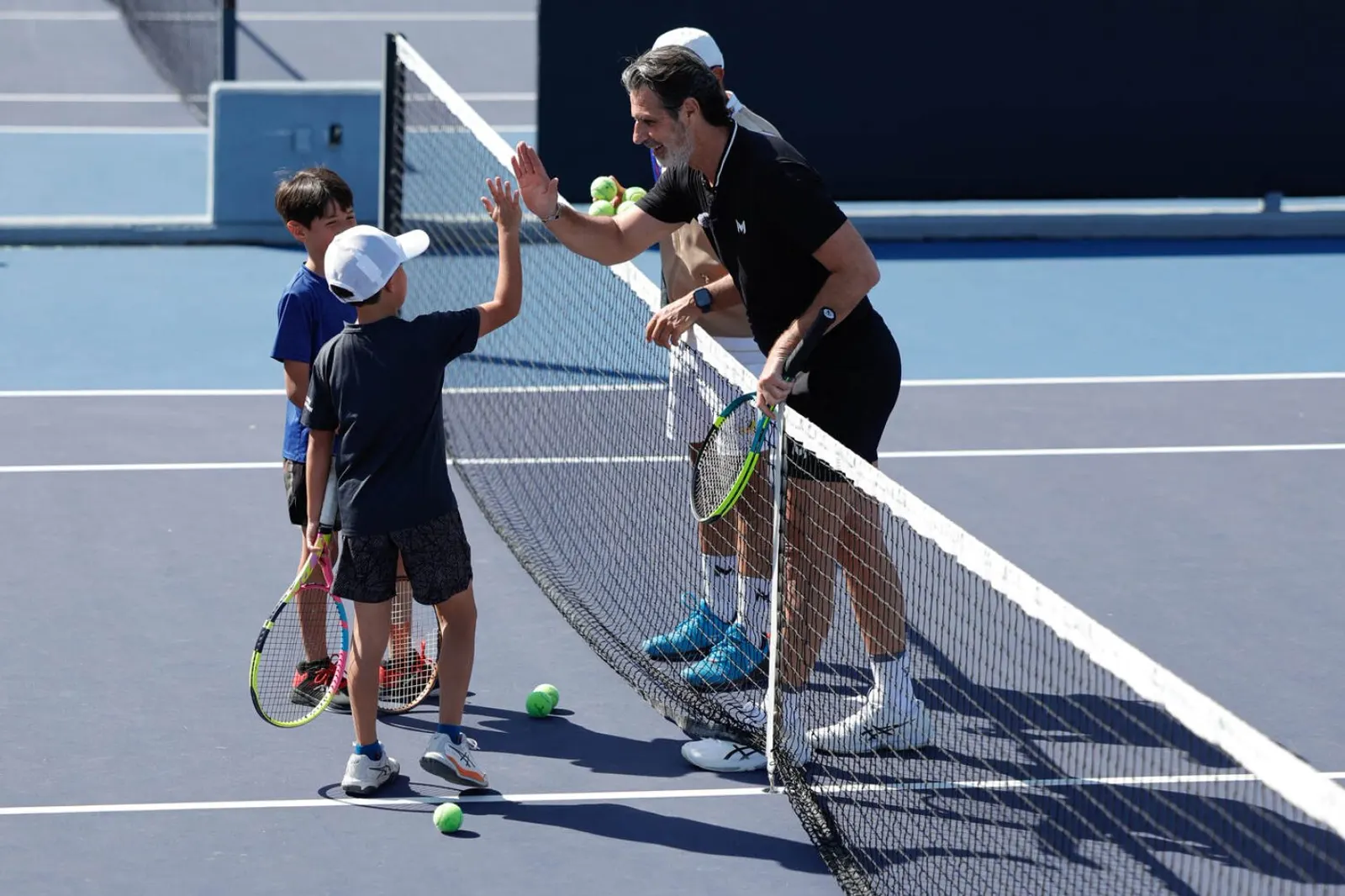 Entrenador chocando la mano con jóvenes jugadores al otro lado de la red en el Mouratoglou Tennis Center Guadalajara