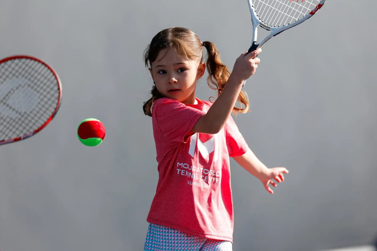 Niña preparándose para golpear una pelota roja blanda con su raqueta en Guadalajara
