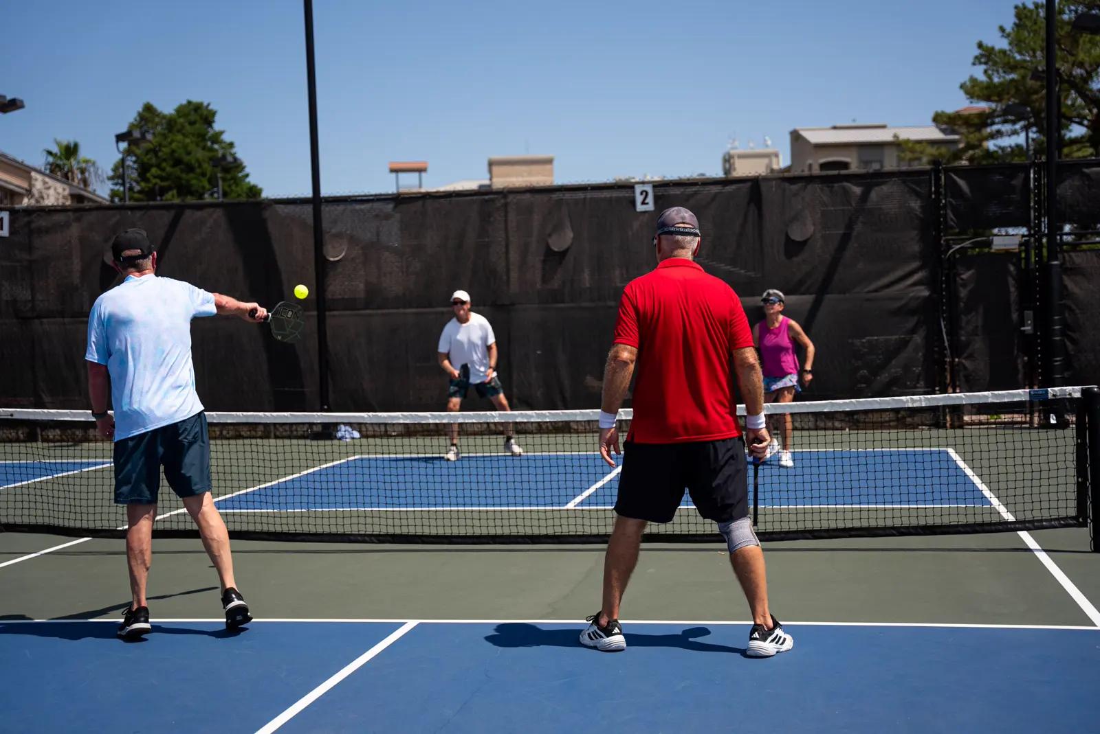 Cuatro adultos jugando un partido de dobles en una pista exterior de pickleball del Mouratoglou Tennis Center Horseshoe Bay.