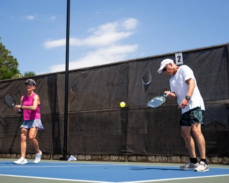 Dos adultos jugando al pickleball en una pista exterior del Mouratoglou Tennis Center Horseshoe Bay bajo el sol.
