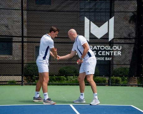 Un entrenador de tenis y un jugador en una pista exterior del Mouratoglou Tennis Center Horseshoe Bay, intercambiando golpes durante un entrenamiento.
