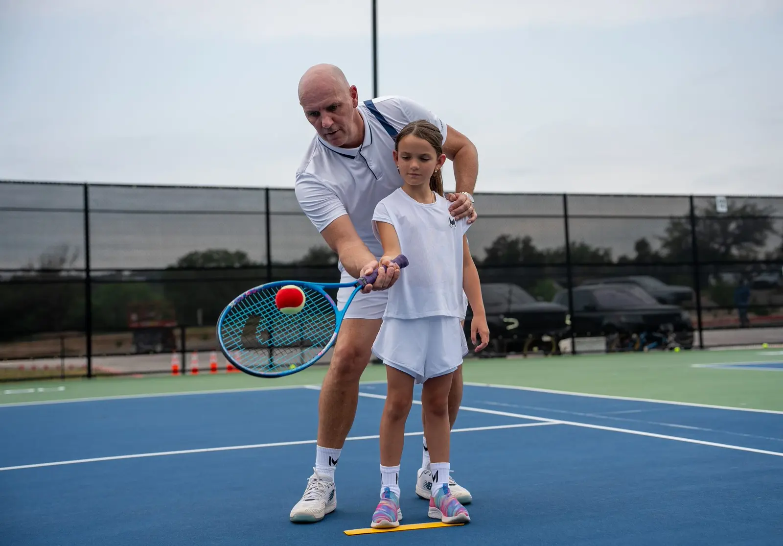 Un niño recibiendo una clase de tenis en una pista exterior