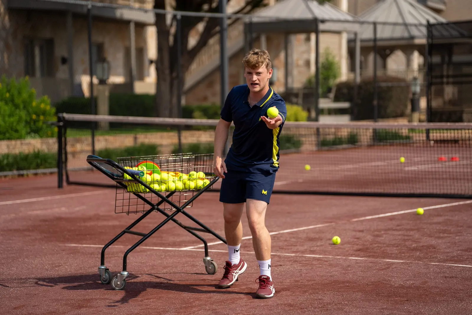 Tennistrainer spielt einen Ball auf einem Sandplatz zu